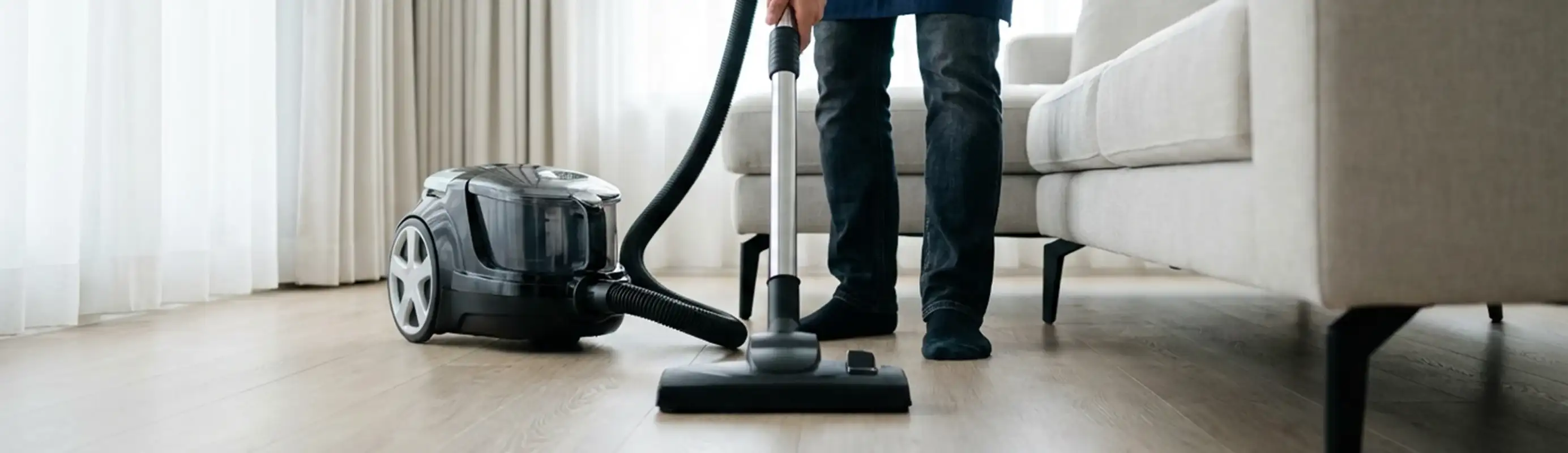 Professional house cleaner vacuuming a living room floor with a canister vacuum cleaner, Yonkers, NY.