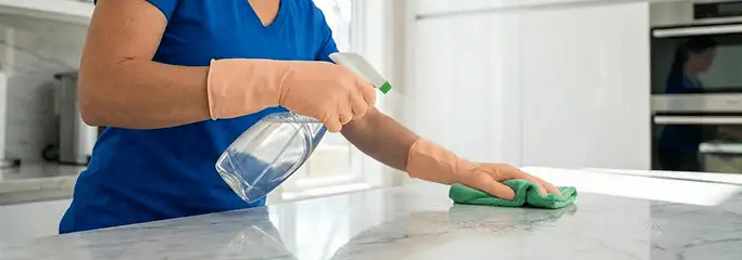 Maid service worker spraying and wiping a kitchen countertop with a microfiber cloth for sanitizing, Yonkers, NY.