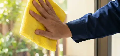 House cleaner wiping a glass window with a yellow microfiber cloth for streak-free cleaning, Yonkers, NY.
